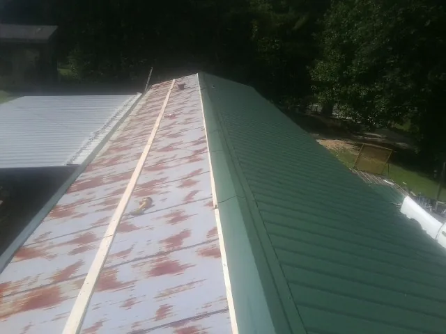 Old rusted panels beside newly installed green metal roofing — Wind Damage Roof Repair by Roofing Brothers in Harrison