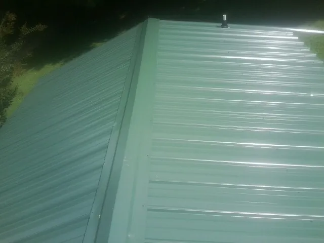 New green metal panels meeting at the ridge of a roof — Flat Roof Repair work by our crew in Harrison