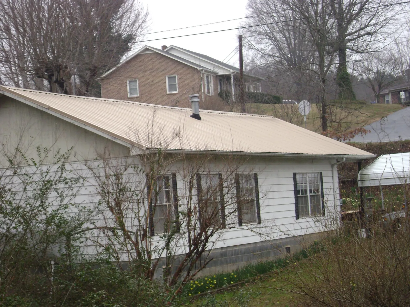 Tan metal roof on a white sided house set into a hillside — Commercial Roofing by Roofing Brothers in Harrison